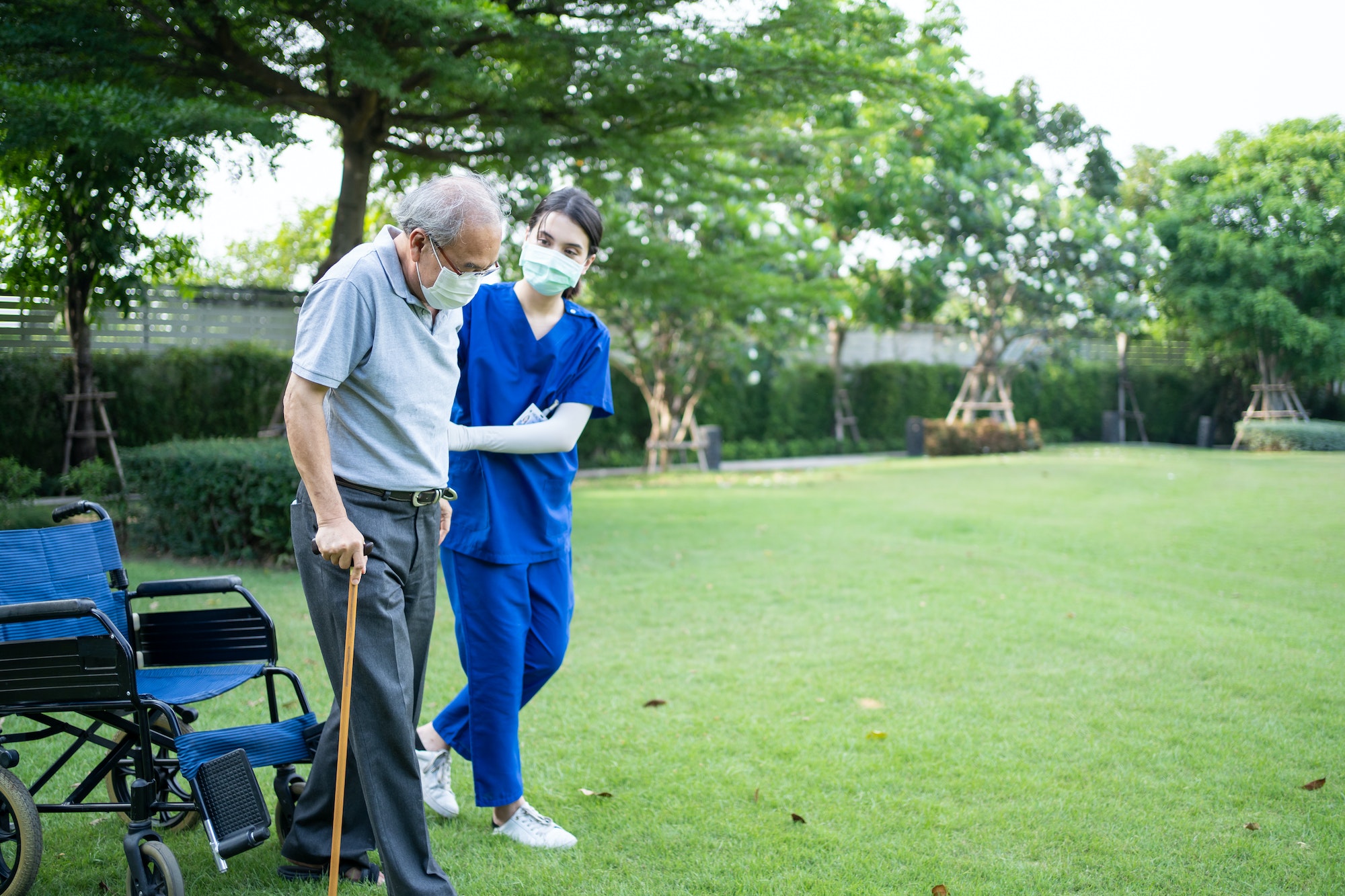 Asian young woman nurse support disabled senior elderly man on wheelchair at backyard.